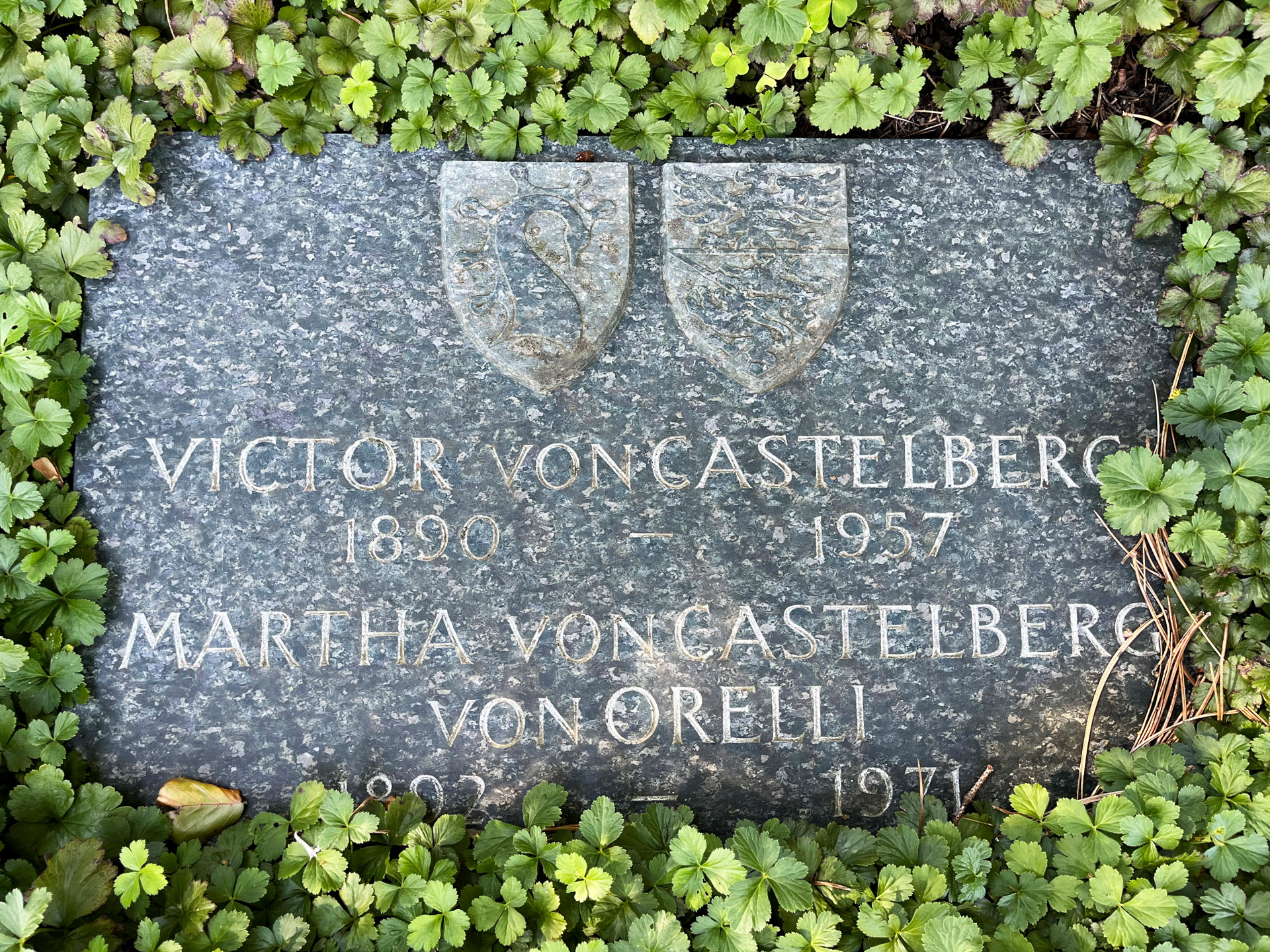 Grabplatte von Martha (1892–1971) und Victor von Castelberg (1890- 1957). Im oberen Teil die Wappen der Familien von Castelberg und von Orelli.